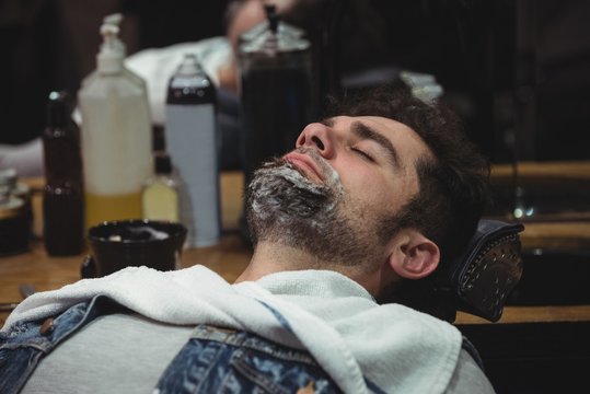 Man with shaving cream on beard relaxing on chair