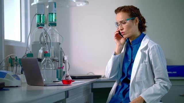 Researcher in lab. Lab woman in laboratory. Female researcher speaking on phone in research lab. Young researcher talking on mobile phone in modern lab. Research development