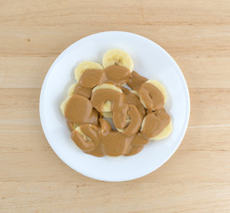 Ripe cut bananas covered with peanut butter on plate top view atop a wood table. 