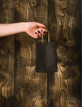 black shopping bag in female hand on wooden background