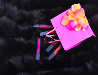 lipsticks with rose petals on present bag on fur background