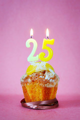 Muffin with burning birthday candles as number twenty five on pink background