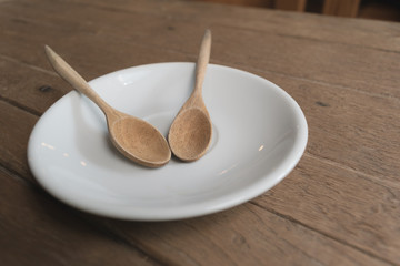 Together wood spoon in white plate on wooden table in the coffee shop.