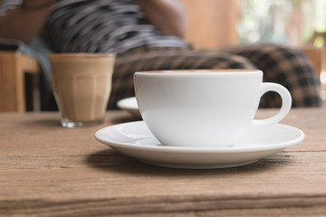 White cup of coffee on wooden table in the coffee shop.