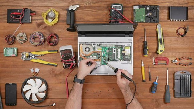 Male engineer solder board laptop at the workplace. Wooden table top view.