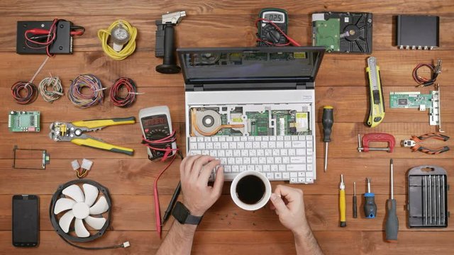 Male engineer computer repair works with disassembled laptop. One can see the computer's motherboard. Wooden table top view