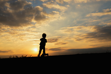 silhouette of a boy,little boy riding scooter at sunset time