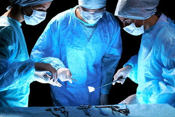 Medical team performing operation. Group of surgeon at work in operating theatre toned in blue.