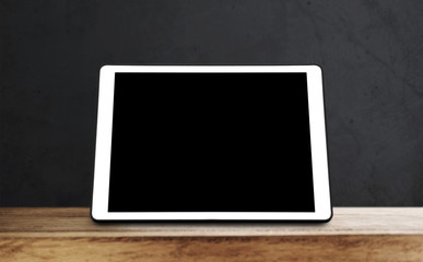 Digital tablet on wooden table, with black wall