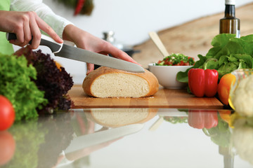 Closeup of human hands slicing bread in kitchen on the glass table with reflection. Healthy meal and vegetarian concept