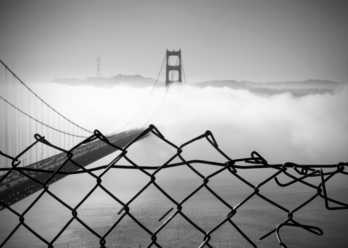 Fototapeta Panoramic view of the western span of the Golden Gate Bridge on a foggy winter morning viewed from Battery Spencer through a fence, a Fort Baker site - black and white rendering.  