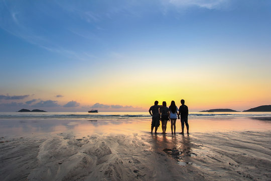 group of happy young people look on beautiful summer sunset at the beach