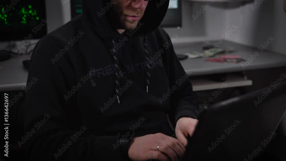 Poster the young hacker on a laptop creates a virus program for cyber attacks on bank server. man in a dark