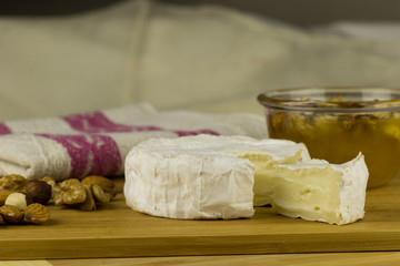 Brie cheese and a slice on a wooden board with nuts, honey. Italian, French cheese.