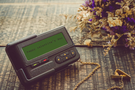 vintage style The message on the pager screen , Happy Valentine's Day with fower on wooden background .