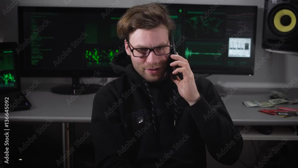 Poster the man in the computer room. young guy with glasses sitting on a chair and talking on his focused s