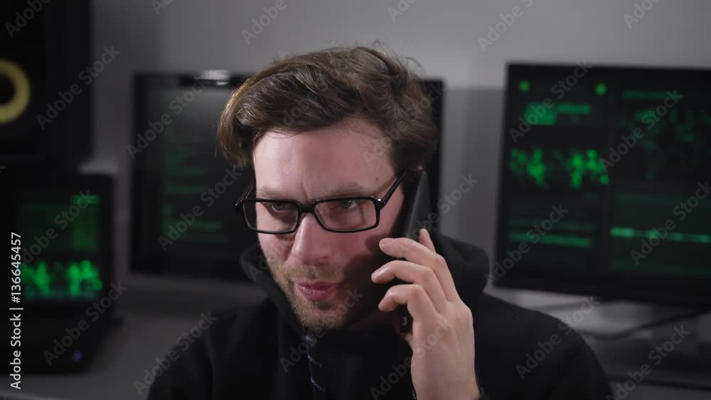 Poster young it professional talking on his mobile phone against a background computers working with e-info