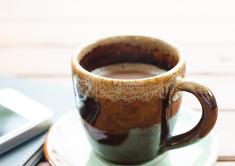 Cup of hot coffee and smartphone on table.