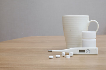 close up soft focus on digital thermometer with medicine bottle and pills on wooden desk for medical concept.