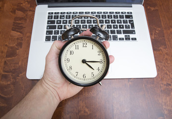 Overtime at work. Get off work and go home. A person is holding a clock showing quarter past four or 0415 and a laptop in the background out of focus.
