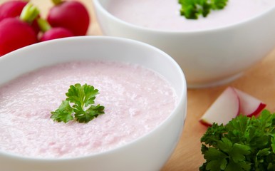 Vegetable radish soup. Bowl of cream radish soup surrounded by ingredients. Wooden background. Closeup view.