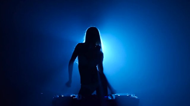 Blonde woman dj plays track and erotically dancing in silhouette