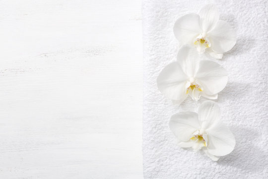 Three orchids and white terry towel  lying on shabby wooden board.  Viewed from above. Spa concept.