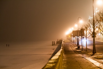 Palace Embankment in the fog on a winter night. Two people on the frozen Neva.