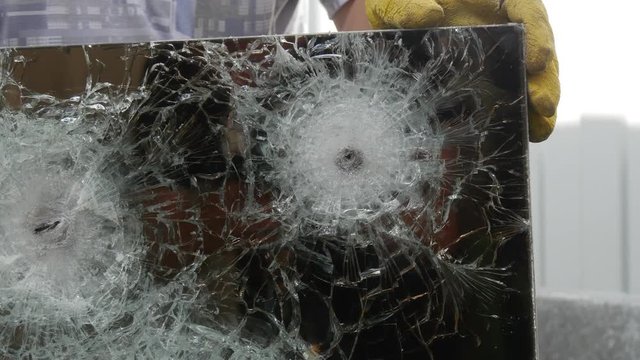 Closeup Shot of Worker`s Hands Keeping a Mirror Looking Glass, Consisting of Several Layers, With Cracks and Fractures From Two Bullets