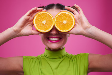Amusing girl holding two parts of orange near eyes