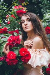 Girl stands against a background bushes with red roses