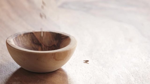 Slow motion of cumin seeds falling in wood bowl on wooden table, 180fps prores footage