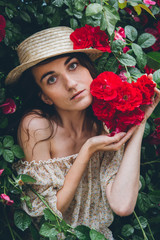 Girl stands against a background bushes with red roses