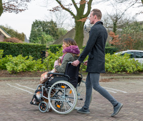 Fototapeta premium Man pushing a woman in a wheelchair at a car park