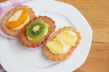 Tortine alla crema e frutta su piatto su tavolo di legno