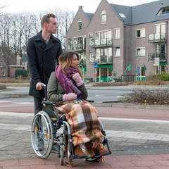 Man pushing a woman in a wheelchair at a  zebra crosssing