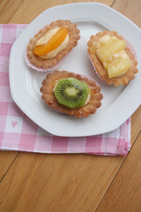 Tortine alla crema e frutta su piatto su tavolo di legno