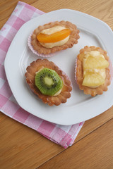 Tortine alla crema e frutta su piatto su tavolo di legno