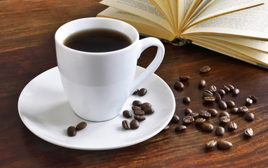 Breakfast scene with coffee cup, open book and coffee beans on a wooden table. Morning scene with hot coffee.