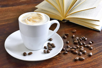 Breakfast scene with coffee cup, open book and coffee beans on a wooden table. Morning scene with hot coffee.