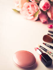 Make up products lipstick, blush and tools brushes with pink roses flowers on white background. Lifestyle woman still life