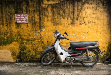 Obraz na płótnie Canvas Old scooter illegally parked in front of rough yellow wall