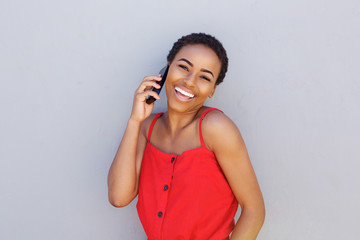smiling black woman talking on cellphone against gray wall
