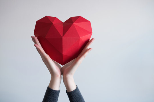 Two female hands holding red polygonal paper heart shape
