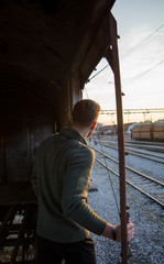 Fit guy in green sweater traveling in old rusty train looking at sunset