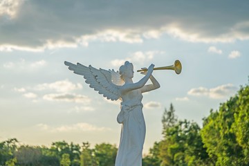 sculpture of angel blowing golden horn on sunrise sky clouds with trees.
A trumpeting golden music...