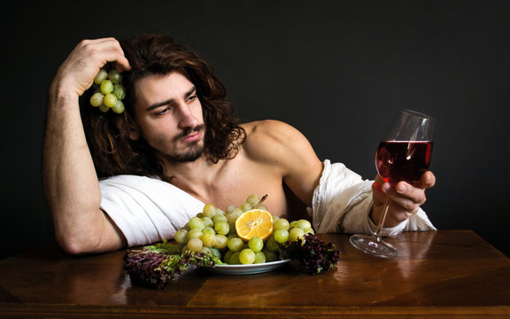 photo portrait of a handsome guy with long curly hair at the table with glass of red drink and a plate of grapes