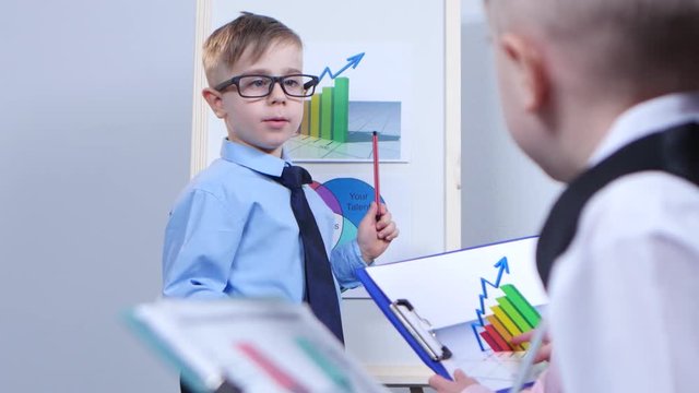 Small businessman pointing to charts, sitting next to children and consider diagram