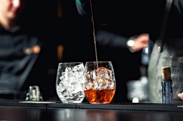 Closeup of bartender hands pouring alcoholic drink into a jigger to prepare a cocktail, with red...