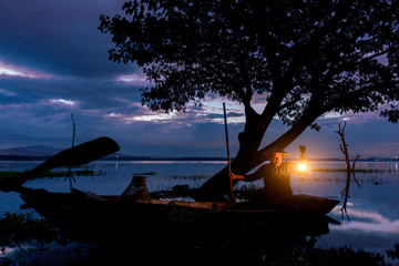 Asian Fisherman on boat fishing at lake  with a lighted lamps.